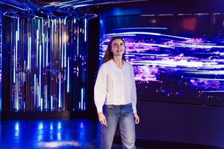 A person standing in a room with vertical light strips and a digital display in the background. 5