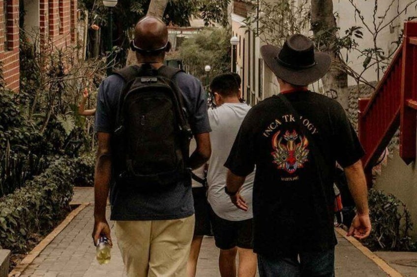 Three people walking on a narrow path surrounded by greenery and buildings. 4