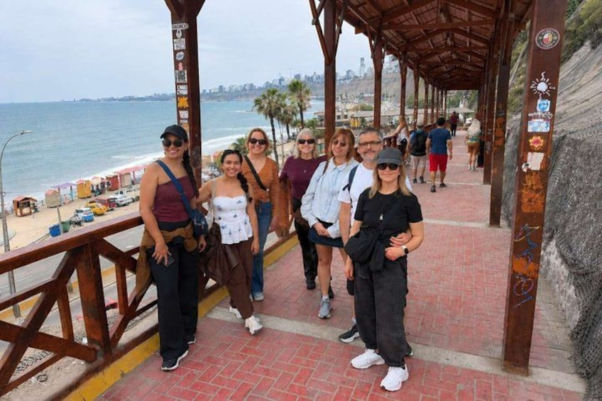 A group of people on a wooden walkway by the beach with a cityscape in the background. 2