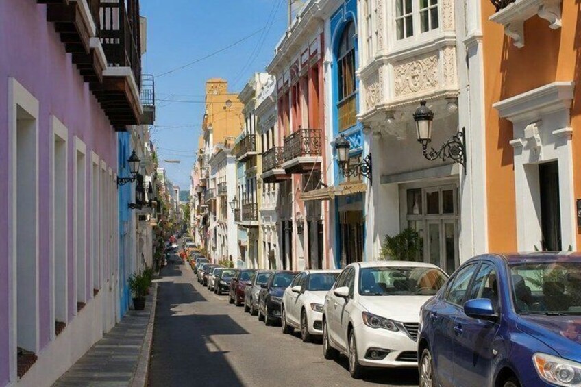 A narrow street lined with colorful buildings and parked cars. 2