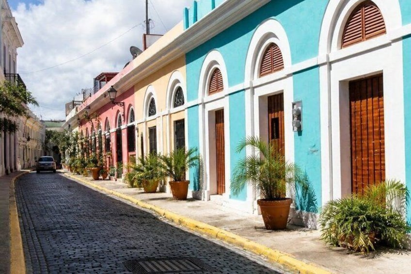 A cobblestone street lined with colorful buildings, potted plants, and a parked car. 4