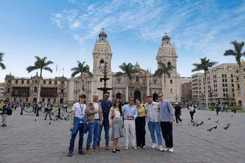A group of people posing in front of a historic building with two prominent towers. 1