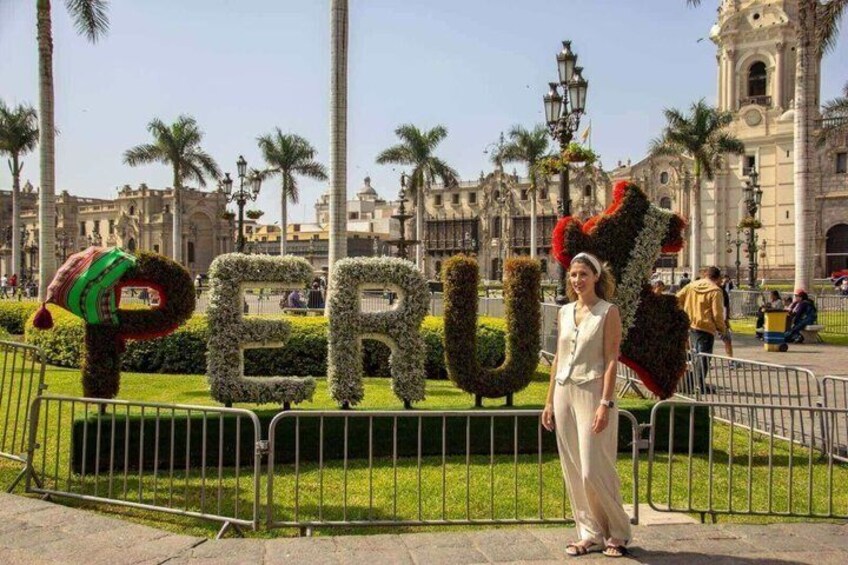 A person standing in front of a large, landscaped sign spelling 'PERU' with a person in a red and green outfit on top. 3