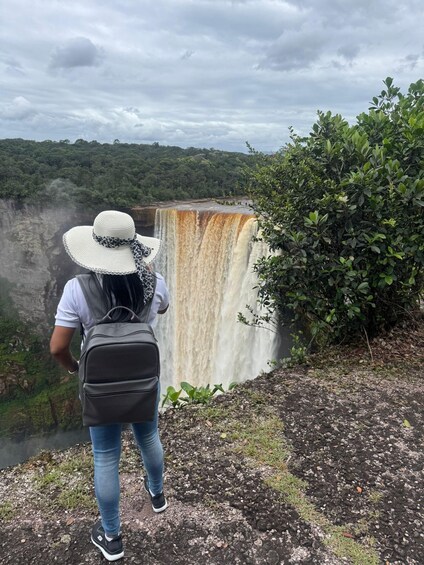 A person standing on a rocky ledge overlooking a waterfall. 1