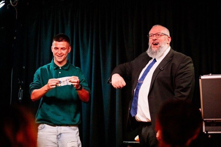 Two men on a stage, one holding a card and the other gesturing. 4