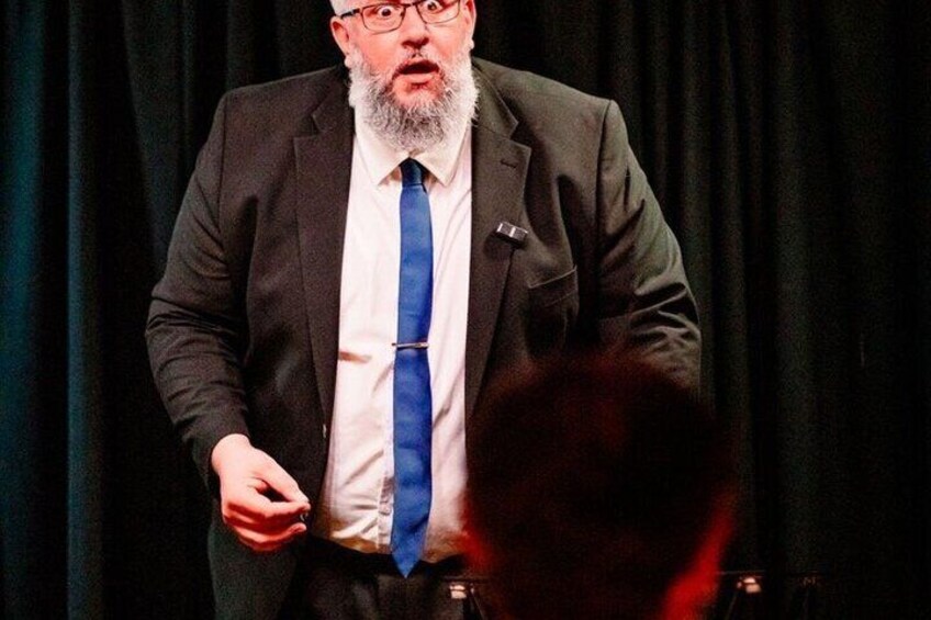 A man in a suit with a blue tie standing on a stage with a microphone. 2