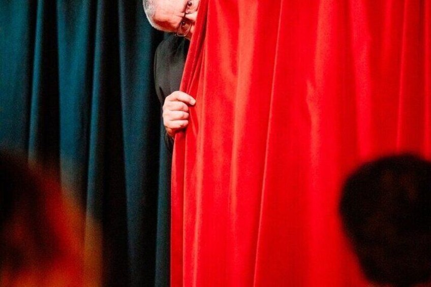 A person peeking from behind a red curtain. 3