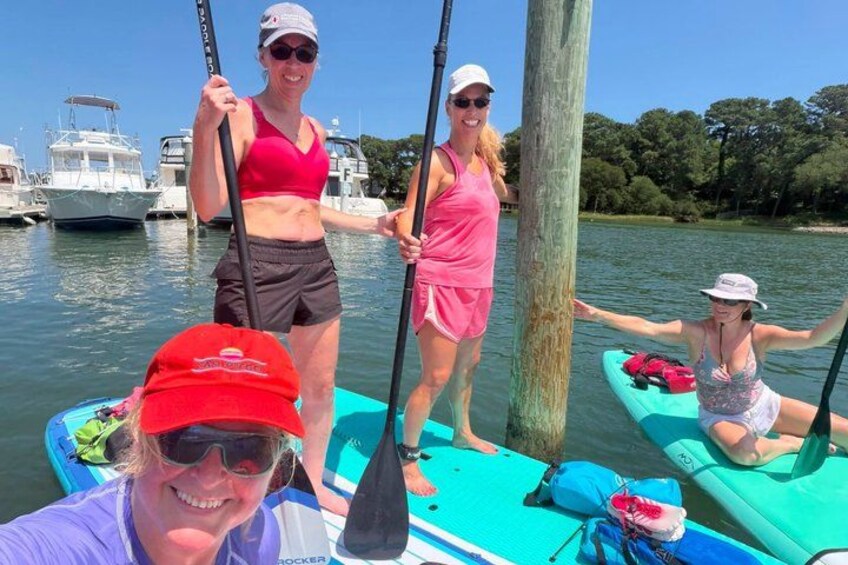 People on paddleboards in a calm body of water with boats in the background. 3