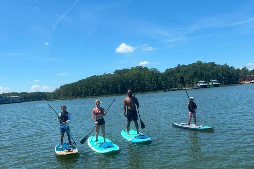 Four people paddleboarding on a calm lake with a forested shoreline in the background. 3