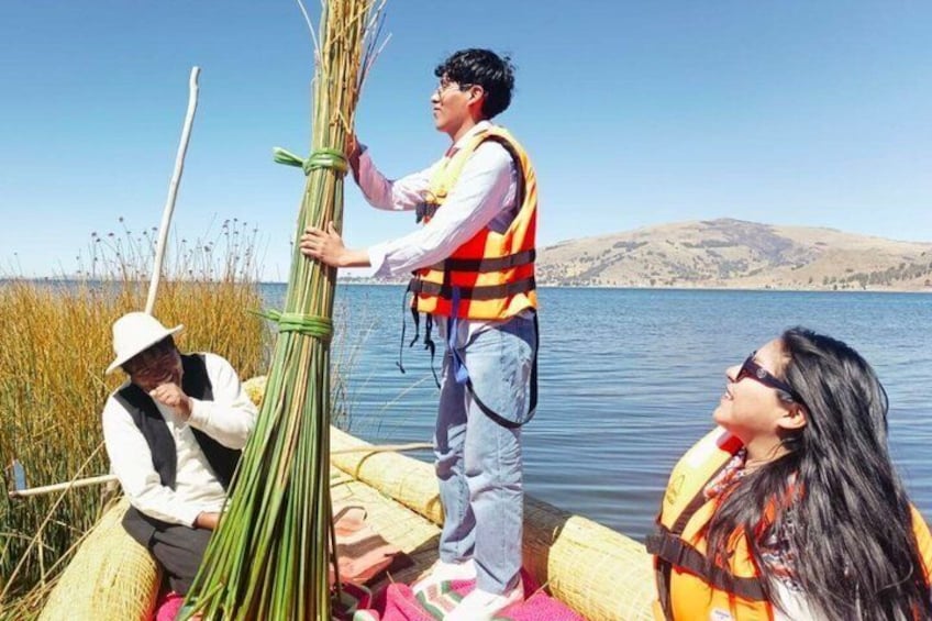 People on a boat near a lake with reeds and hills in the background. 1