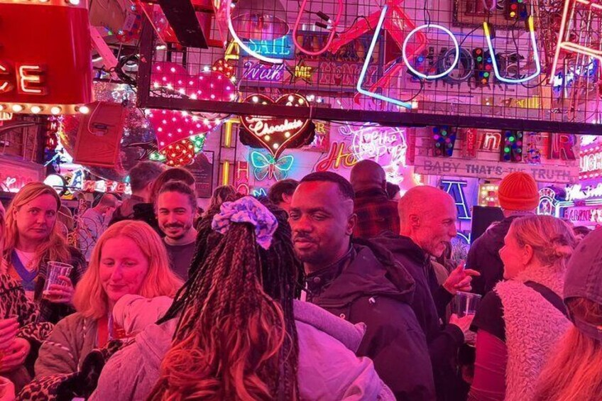 A crowded indoor space with neon signs and lights. 1
