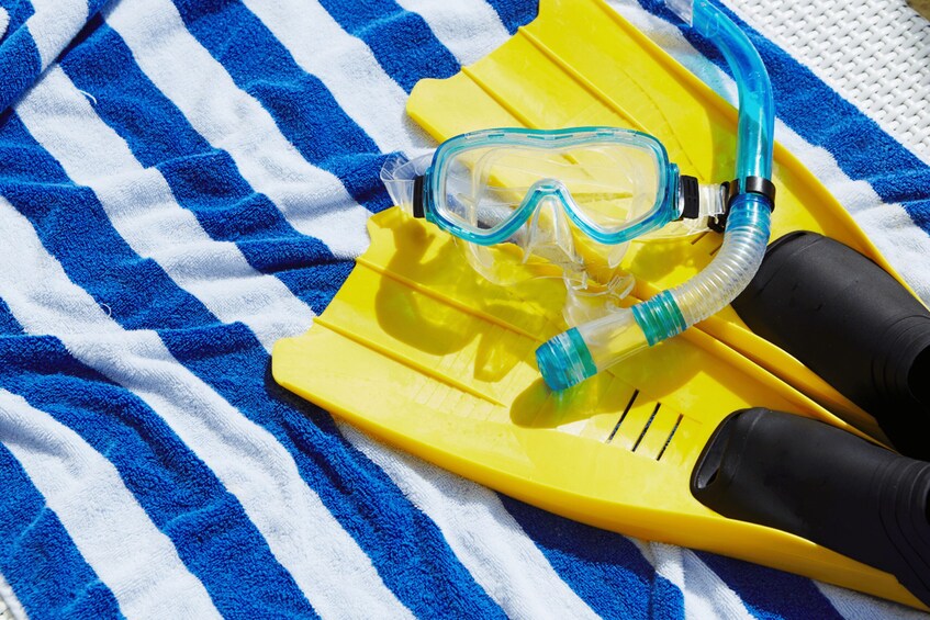 A pair of yellow snorkeling fins and a snorkel on a blue and white striped towel. 2