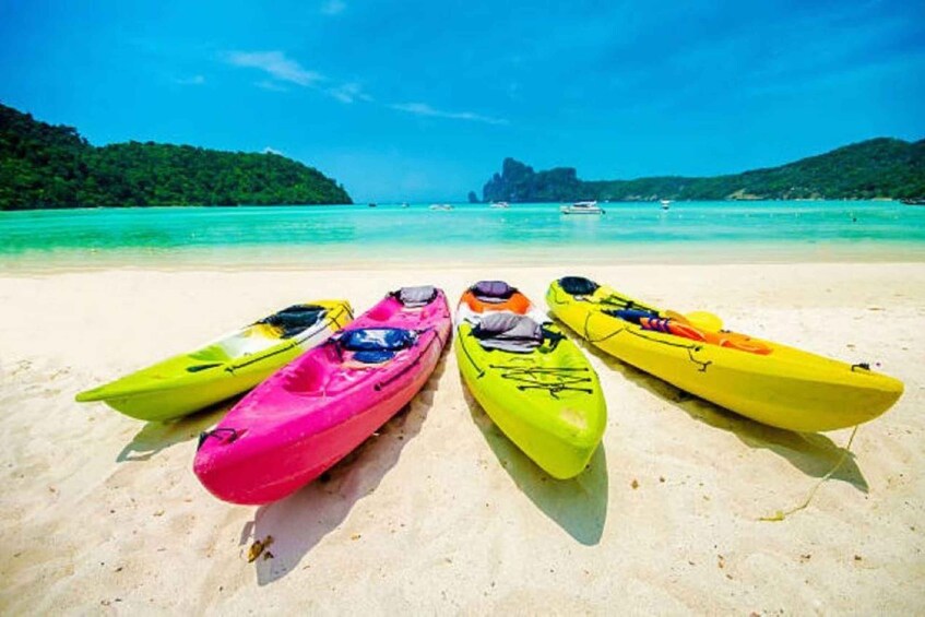 Four kayaks on a sandy beach with turquoise water and green hills in the background. 3