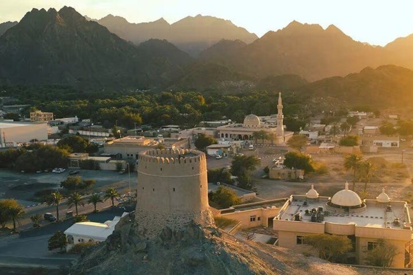 A fortified tower, a mosque with a minaret, and a mountainous backdrop. 1
