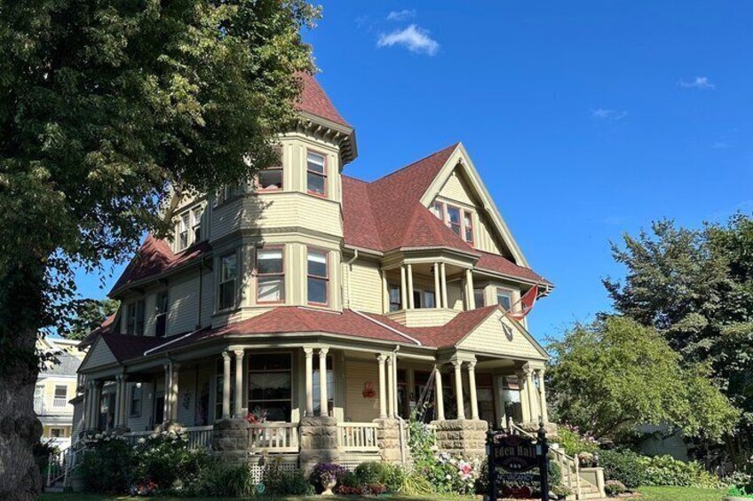 A large, historic house with a prominent tower, a wrap-around porch, and a red roof. 5