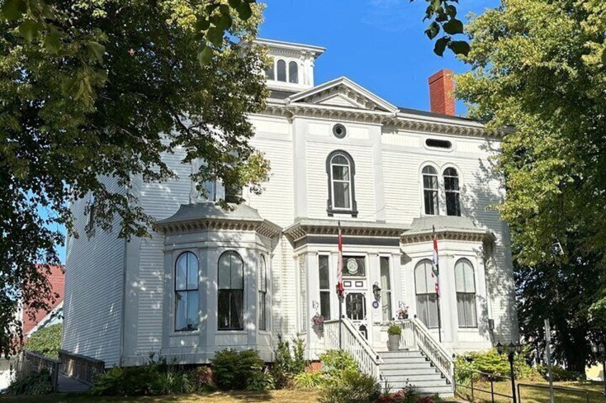 A white historic building with a central entrance, arched windows, and a red brick chimney. 4