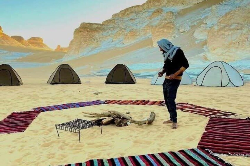 A desert camping scene with tents, a fire pit, and a person standing. 4