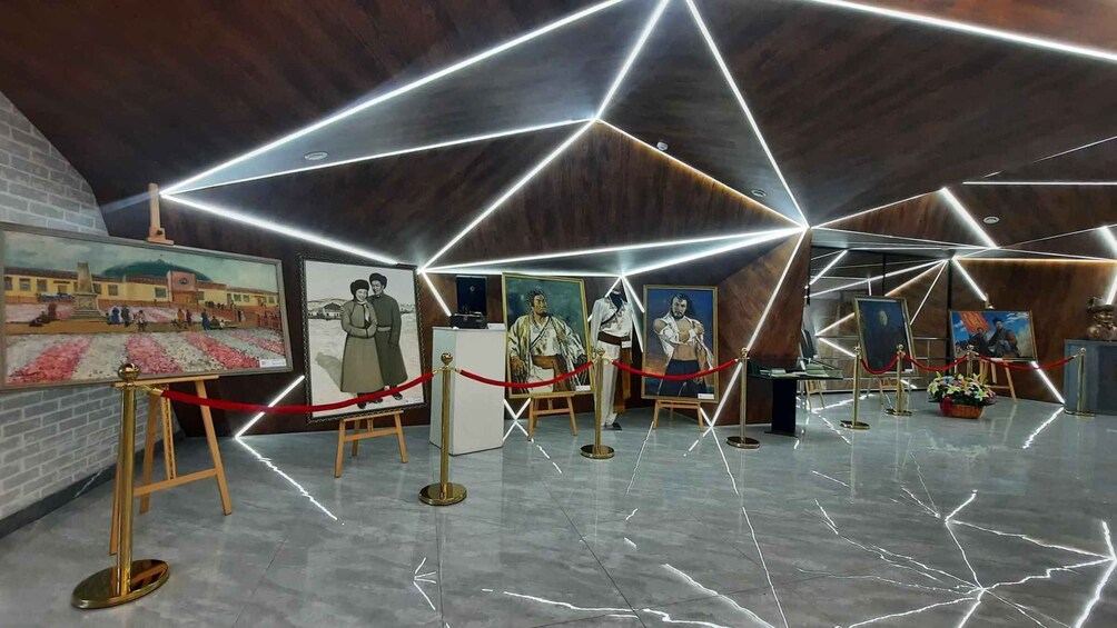 An art exhibition with paintings on easels, red ropes, and geometric light patterns on the ceiling. 4