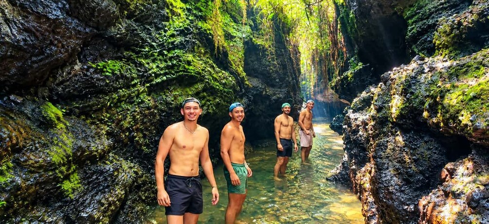 A group of people standing in a narrow, rocky waterway surrounded by lush greenery. 3