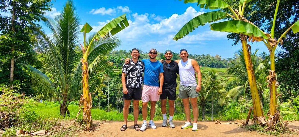 Four people standing in a tropical setting with banana trees and lush greenery. 2