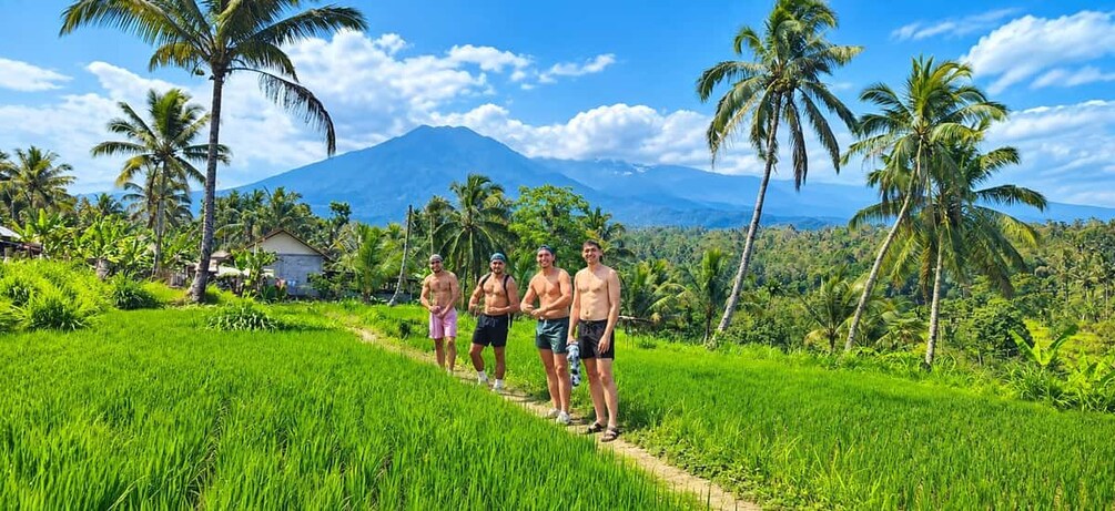 A group of people standing on a path in a lush green field with palm trees and a mountain in the background. 4