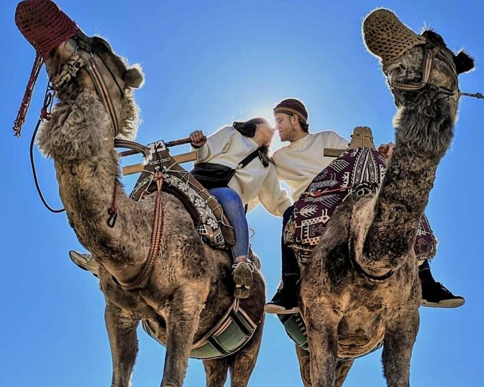 Two camels with riders, a clear blue sky in the background. 3