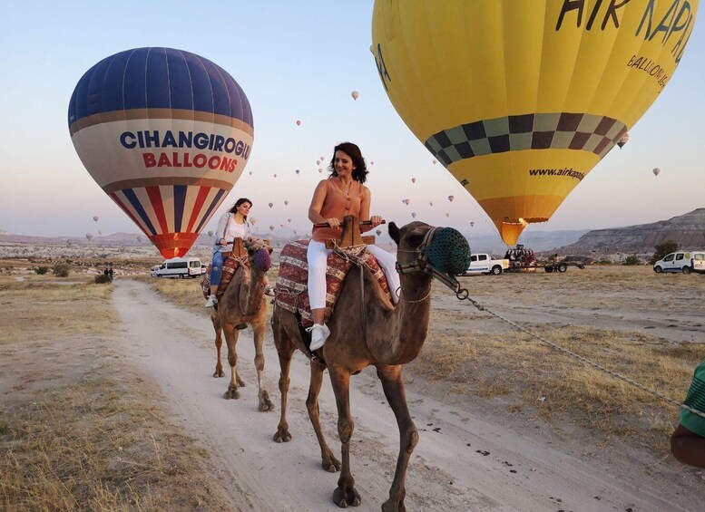 A desert landscape with people riding camels and hot air balloons in the background. 1