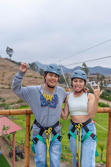 Two people wearing helmets and harnesses, standing on a rope bridge with a mountainous landscape in the background. 4