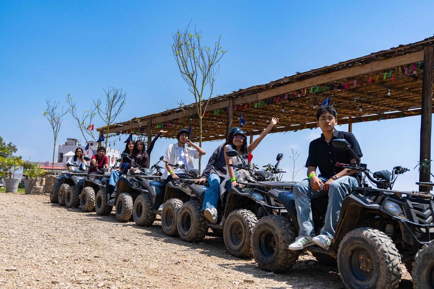 A group of people on ATVs lined up under a wooden shelter with colorful flags. 3