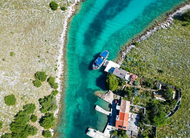 An aerial view of a coastal area with clear turquoise waters, a boat docked near a building, and surrounding vegetation. 1
