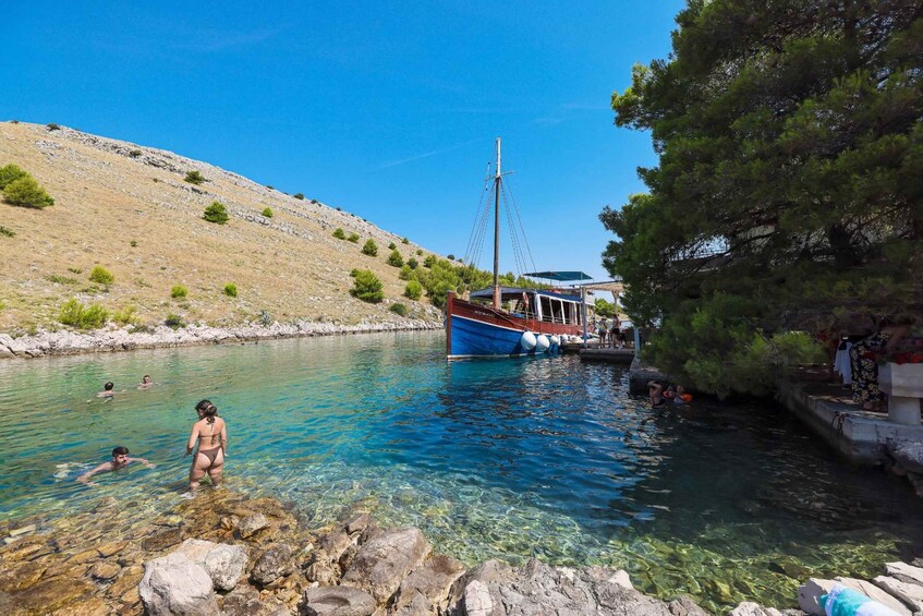 A clear blue body of water with people swimming and a boat docked at the shore. 2