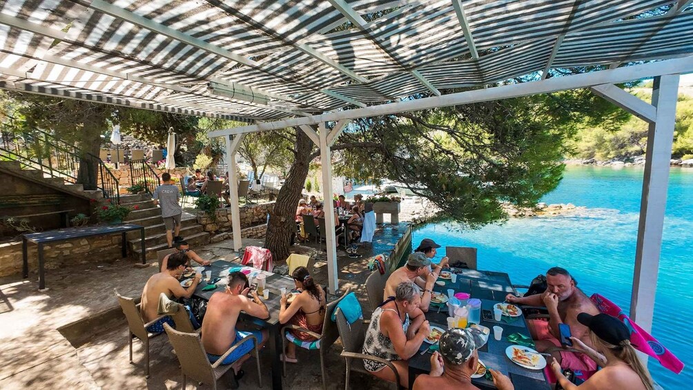 A poolside dining area with people eating and socializing under a shaded pergola. 4