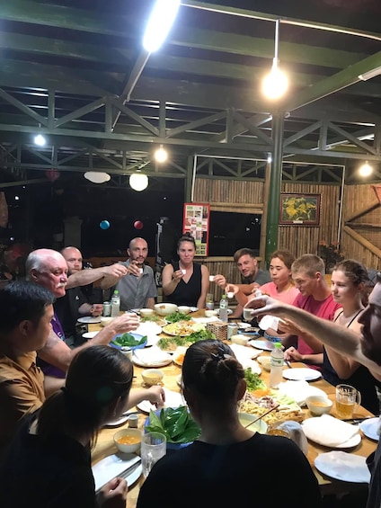 A group of people dining at a wooden table with various dishes and drinks. 2