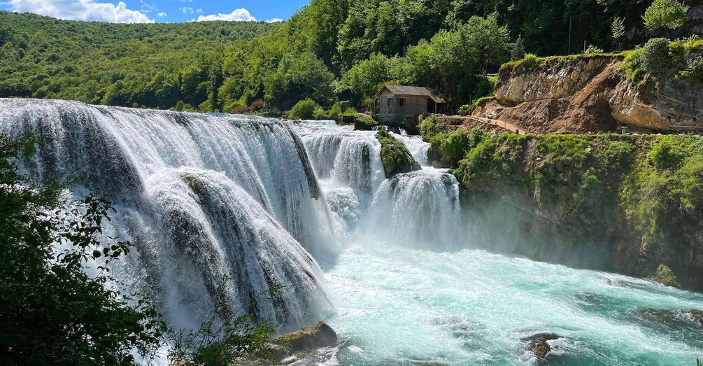 A waterfall cascading over rocks, surrounded by lush greenery and a small building. 1