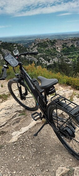 A black electric mountain bike parked on rocky terrain with a scenic view of a valley and ruins in the background. 5