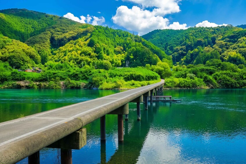 A concrete bridge over a calm river with lush green hills in the background. 3