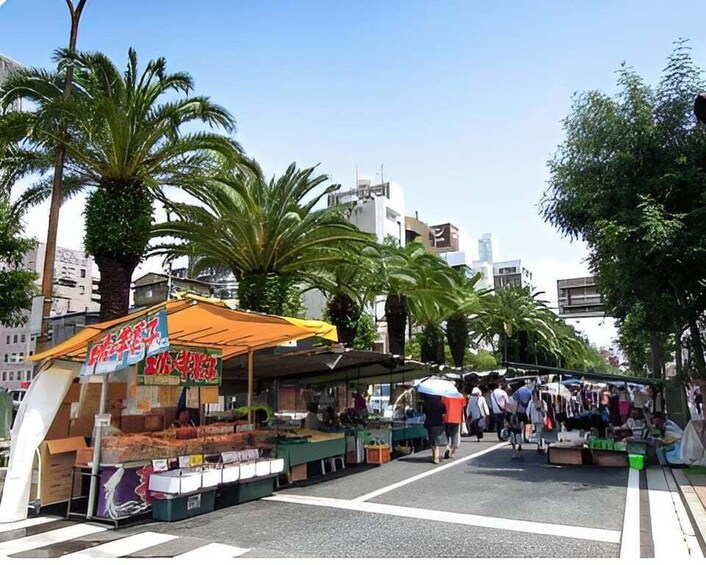 A street market with stalls selling goods, palm trees, and buildings in the background. 5