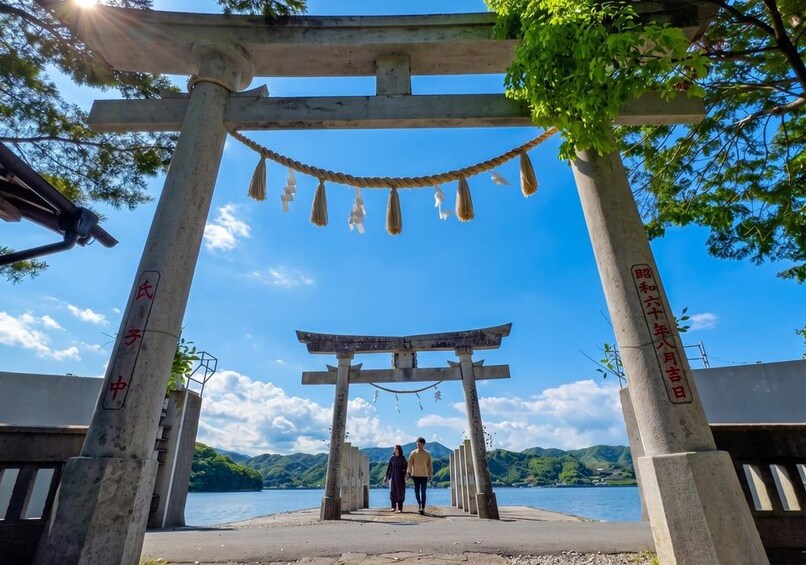 A traditional Japanese torii gate with two people walking through it, overlooking a lake with mountains in the background. 2