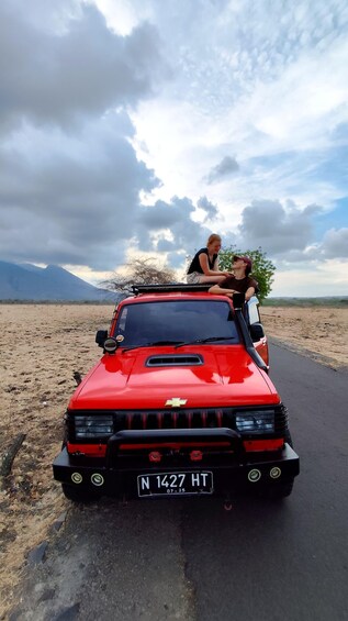 A red Chevrolet car with two people on the roof, parked on a road with a desert landscape and mountains in the background. 3