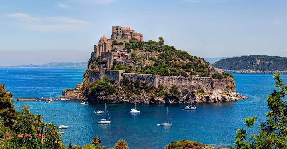A historic fortified island with a castle, surrounded by clear blue waters and anchored boats. 3