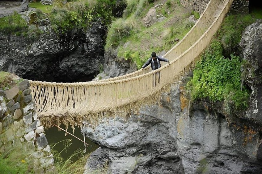 A person walking on a rope bridge over a rocky river. 3
