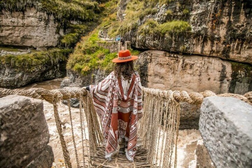 A person standing on a rope bridge over a canyon with rocky cliffs and greenery. 2