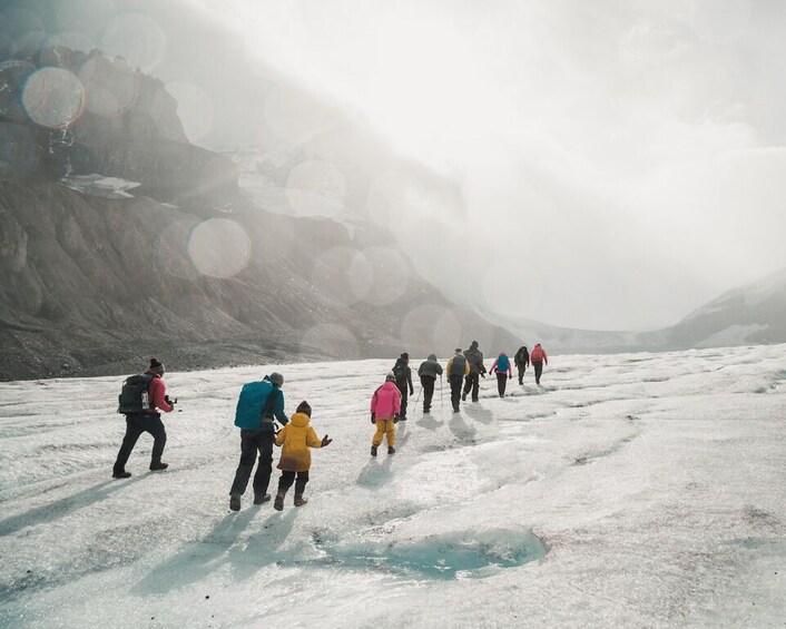 A group of people hiking on a glacier with a mountainous backdrop. 5