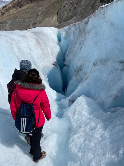 Two people walking through a snow-filled crevasse with a mountain in the background. 3