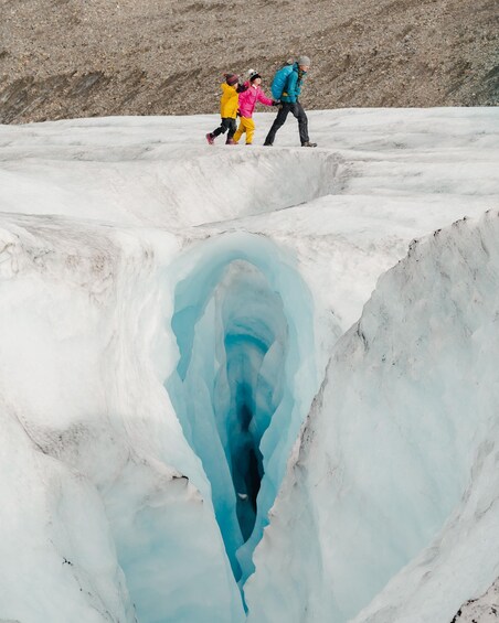 A glacier with a crevasse and people walking on the ice. 4