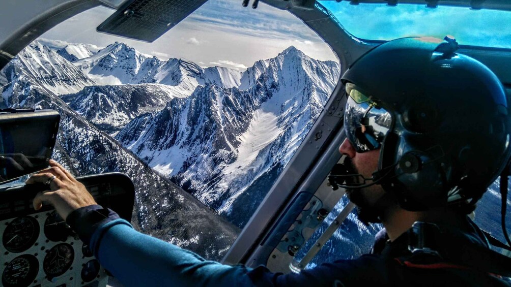 A pilot inside a helicopter with a snowy mountain range in the background. 4