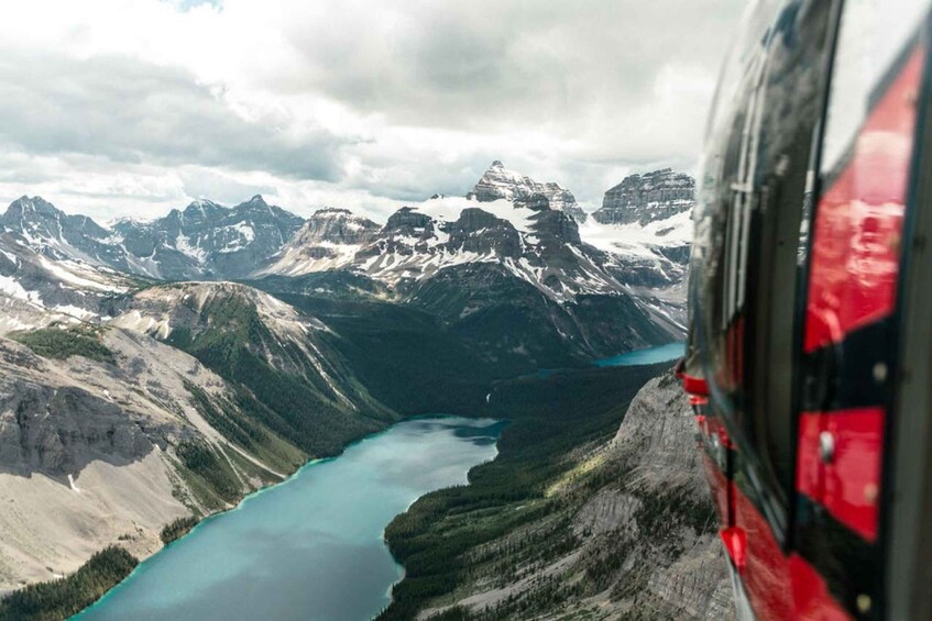 A helicopter view of a mountainous landscape with a turquoise lake and snow-capped peaks. 1