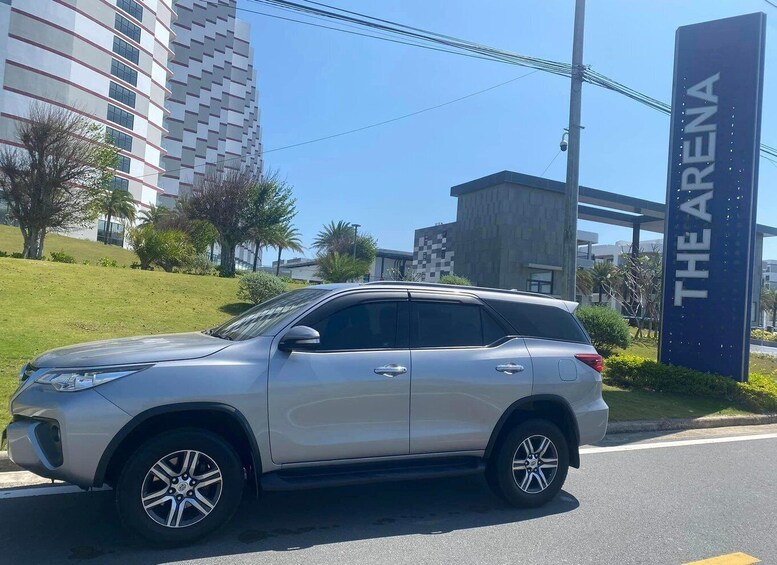 A silver SUV parked on a street with a sign reading 'THE ARENA' in the background. 1
