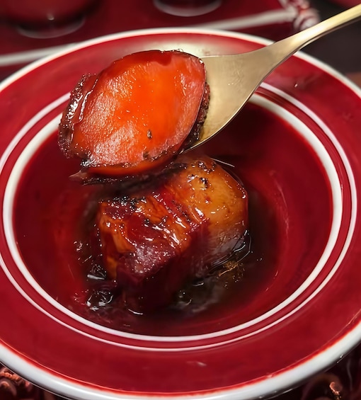 Una cucharada de un postre rojo con superficie brillante y caramelizada, en un tazón rojo y blanco. 5
