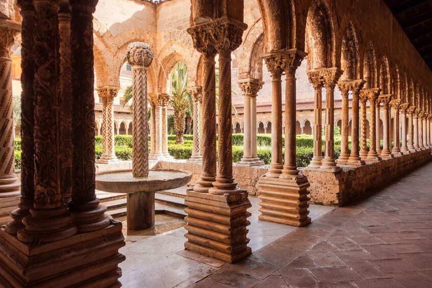 A series of ornate columns in a courtyard with a fountain and palm trees. 3